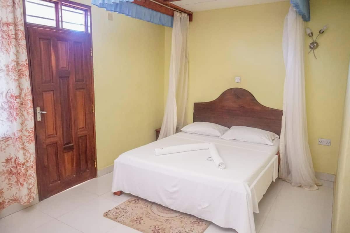 A bedroom with a wooden bed, white bedding, and a patterned rug.