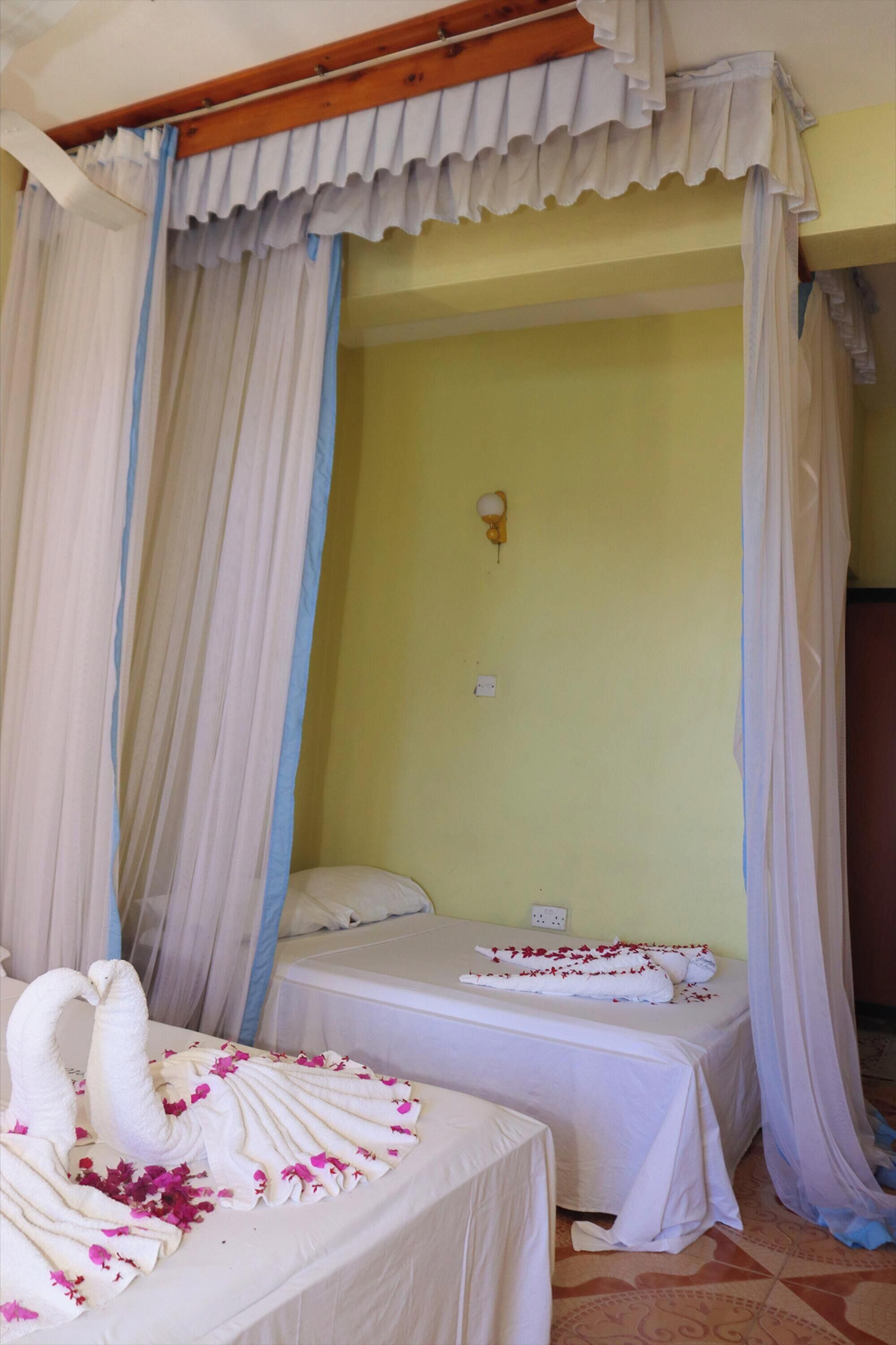 Une chambre avec deux lits, chacun recouvert de draps blancs et décoré de fleurs roses. La chambre a un mur jaune et un plafond en bois.