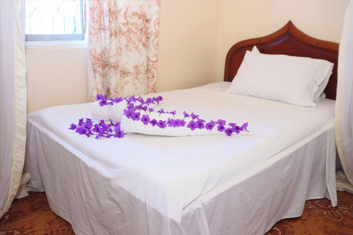 A neatly made bed with white linens and a floral arrangement on the bedspread.