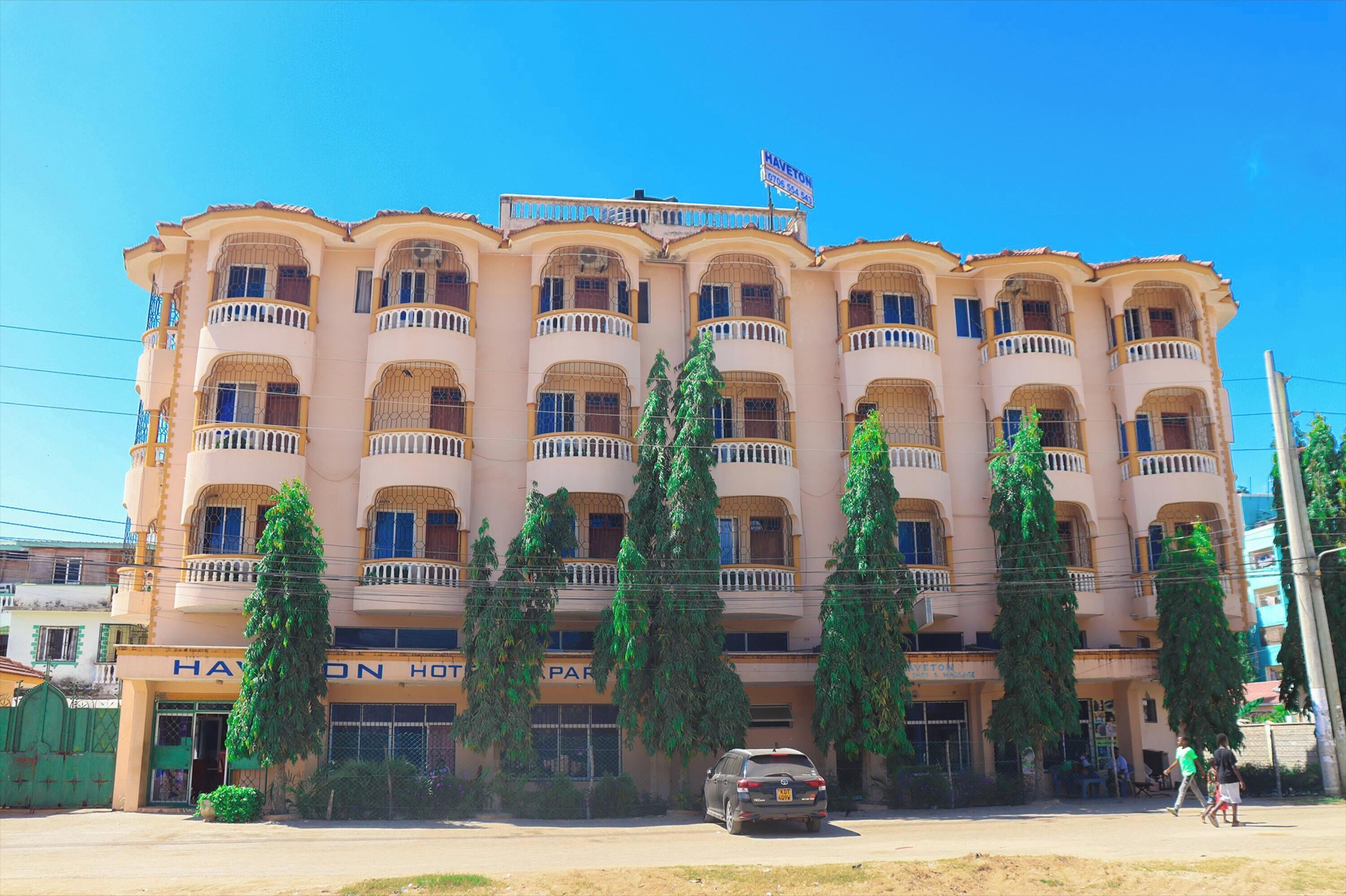A multi-story hotel with balconies, a sign indicating it is a hotel, and a parked car in front.