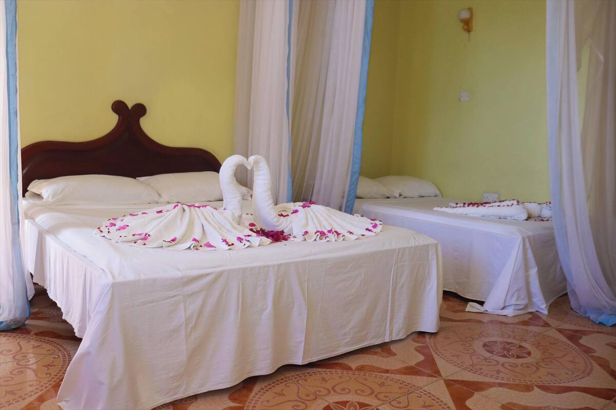 A hotel room with two beds, each with white bedding and a decorative swan made of fabric.
