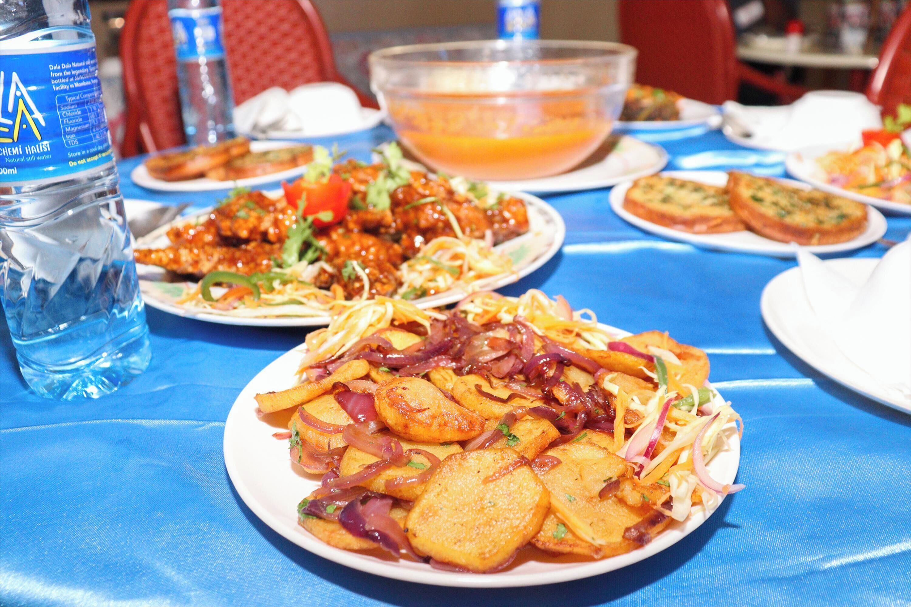 A table set with various dishes, including a plate of potato wedges, a bowl of soup, and a bottle of water.