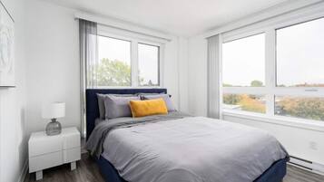 A bedroom with a bed, nightstand, and large windows.