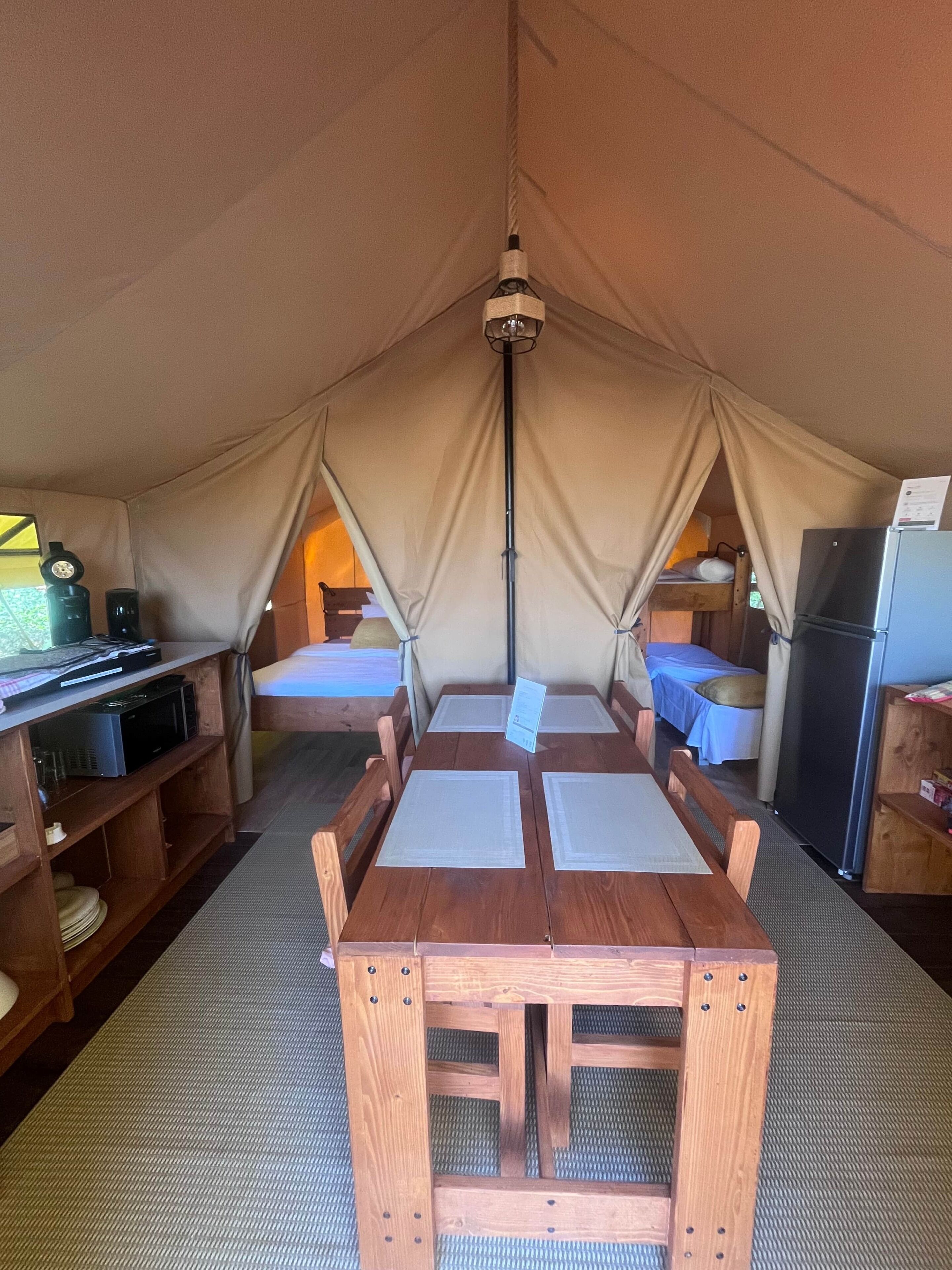A tented accommodation with a wooden table, bunk beds, and a refrigerator.