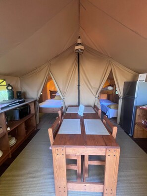 Acomodação em tenda com mesa de madeira, beliches e geladeira.