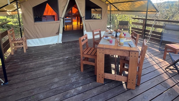 Ett utomhusområde med ett tältliknande tak, en träveranda, ett bord med stolar och utsikt över det omgivande landskapet.