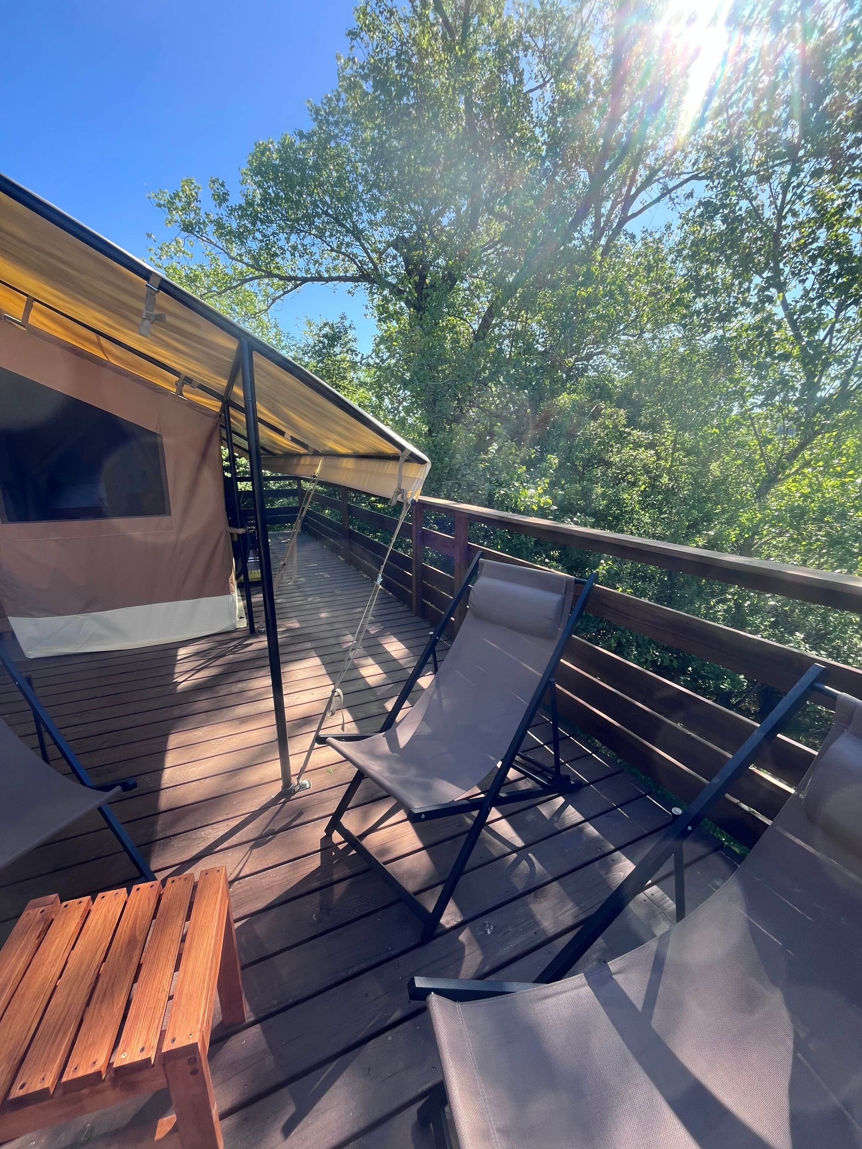 A wooden deck with a covered area, two lounge chairs, and a small table.