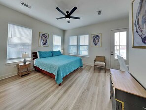 A bedroom with a bed, a chair, a desk, and artwork on the walls. - Oyster & Pearl | Midtown, Coastal Chic (Galveston)