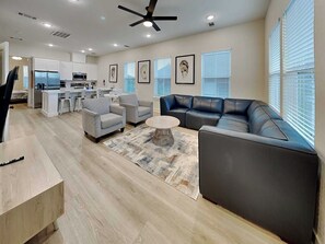 A modern living room with a black leather sofa, two grey armchairs, a coffee table, and a kitchen in the background. - Oyster & Pearl | Midtown, Coastal Chic (Galveston)