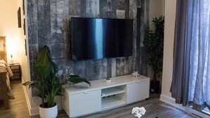 Ein modernes Wohnzimmer mit einem Flachbildfernseher an einer Holzwand, einer weißen Unterhaltungsecke und einer Topfpflanze.