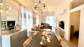 Ein modernes Wohnzimmer mit einem langen Esstisch, Sofas und einem Fernseher.