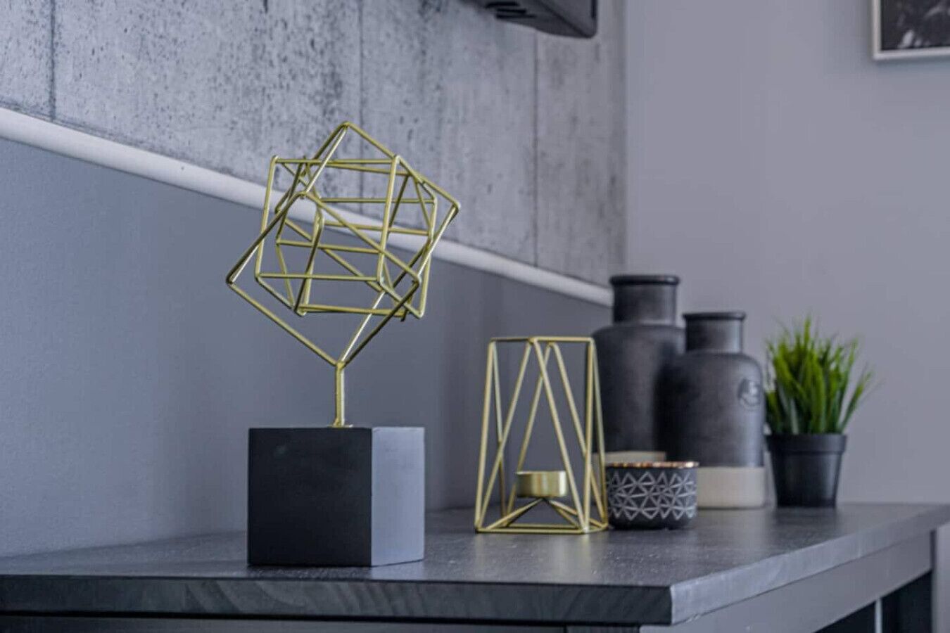 A modern kitchen counter with a geometric metal sculpture, a black and white vase, and a potted plant.