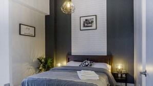 Ett modernt sovrum med en stor säng, två sängbord, en väggmonterad lampa och en inramad tavla.