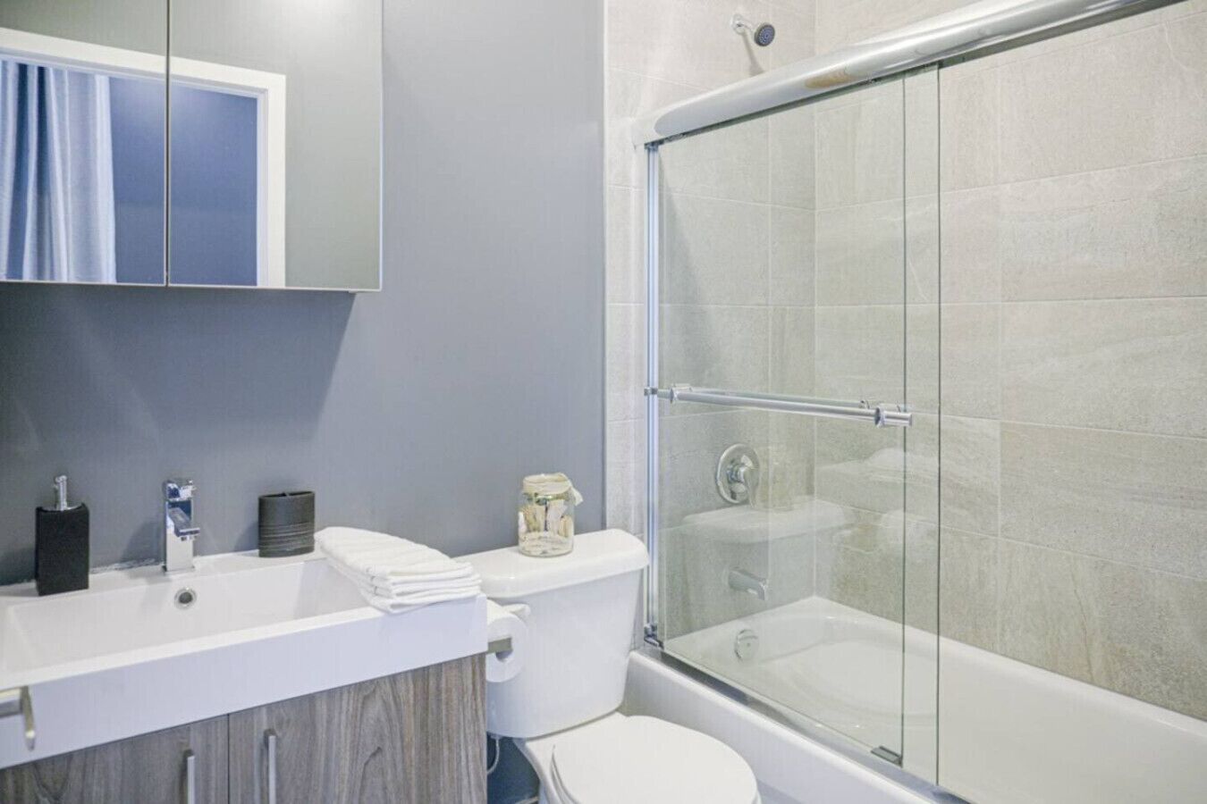 A modern bathroom with a glass-enclosed shower, a white sink with a mirror above, and a toilet.