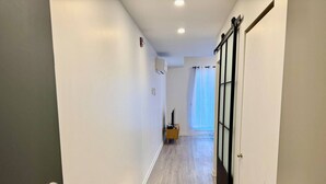 A hallway with a wooden floor, white walls, and a sliding glass door leading to a room.