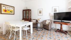 A living room with a white table, white chairs, a brown sofa, a TV, and a cabinet. - Vatican Heart 5 pax 2 bath (Roma)