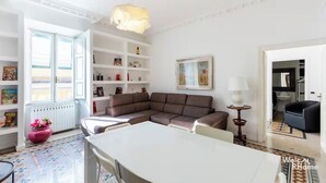 A modern living room with a sectional sofa, a dining table, and a bookshelf. - Vatican Heart 5 pax 2 bath (Roma)