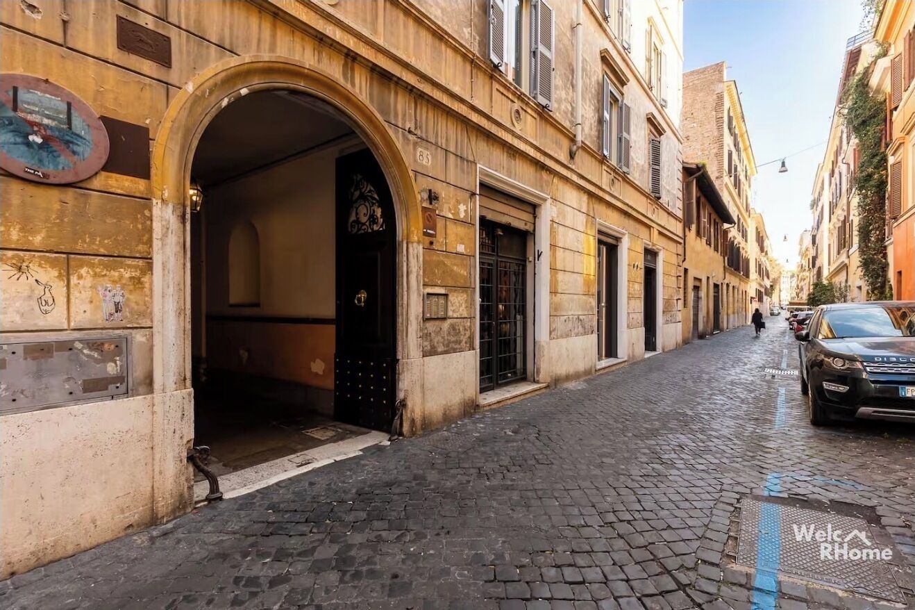 Uma rua estreita de paralelepípedos com edifícios históricos, uma porta à vista e um carro estacionado.