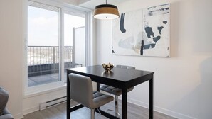 A modern dining area with a dark wooden table, grey upholstered chairs, and a pendant light. A large abstract painting adorns the wall above the table. - Buchanan *609* - Midtown Luxe Loft + gym (Montreal)