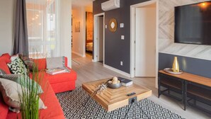 A modern living room with a red sofa, a coffee table, and a TV on a wall. - Buchanan *401* - Midtown Condo Luxe + gym (Montreal)