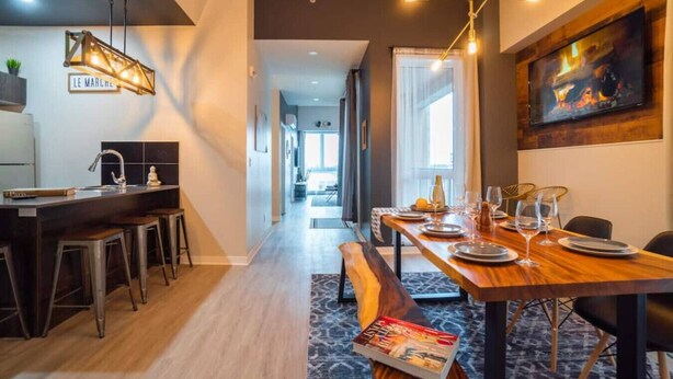 A modern kitchen with a bar area, a dining table set for six, and a fireplace. - Buchanan *401* - Midtown Condo Luxe + gym (Montreal)