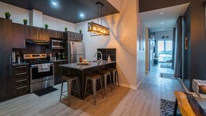 A modern kitchen with dark wood cabinets, stainless steel appliances, and a central island with stools. - Buchanan *401* - Midtown Condo Luxe + gym (Montreal)