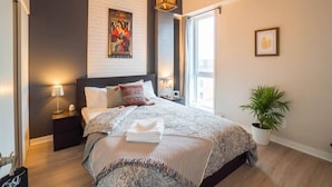 A modern bedroom with a large bed, a nightstand with a lamp, a poster on the wall, and a potted plant. - Buchanan *401* - Midtown Condo Luxe + gym (Montreal)