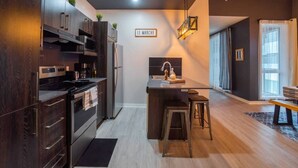 A modern kitchen with dark wood cabinets, stainless steel appliances, and a small island with stools. - Buchanan *401* - Midtown Condo Luxe + gym (Montreal)