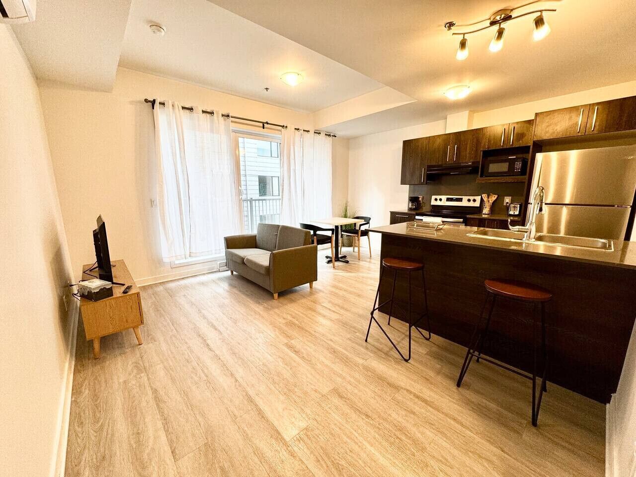 A modern kitchen with dark cabinets, stainless steel appliances, and a bar area with stools.