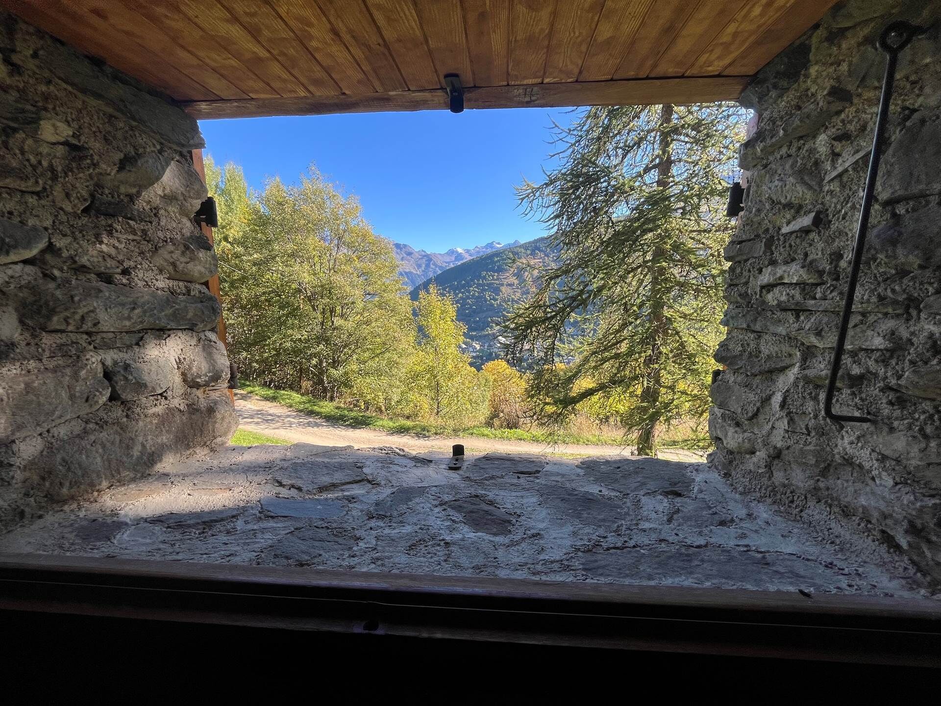 A rustic stone room with a wooden ceiling and a view of a mountainous landscape with trees.