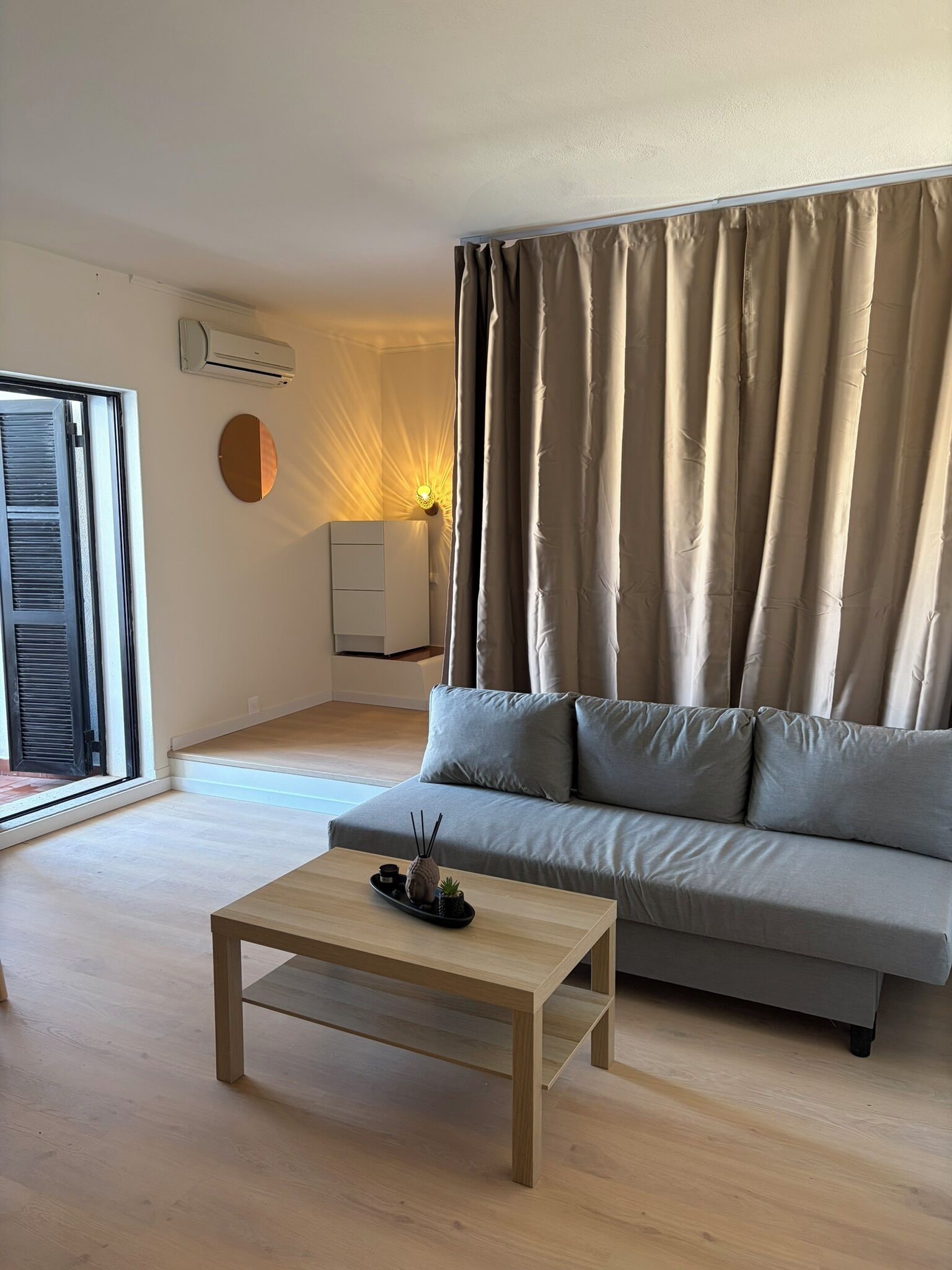 A modern living room with a sofa, a coffee table, and a wall-mounted air conditioner.