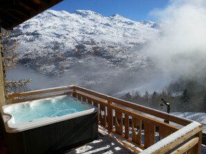 Un bain à remous sur une terrasse en bois, avec une vue sur une montagne enneigée.