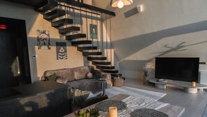 A modern living room with a staircase, a sofa, a coffee table, and a flat-screen TV. - Twin Vista A-Frame Cabins (Sovata)
