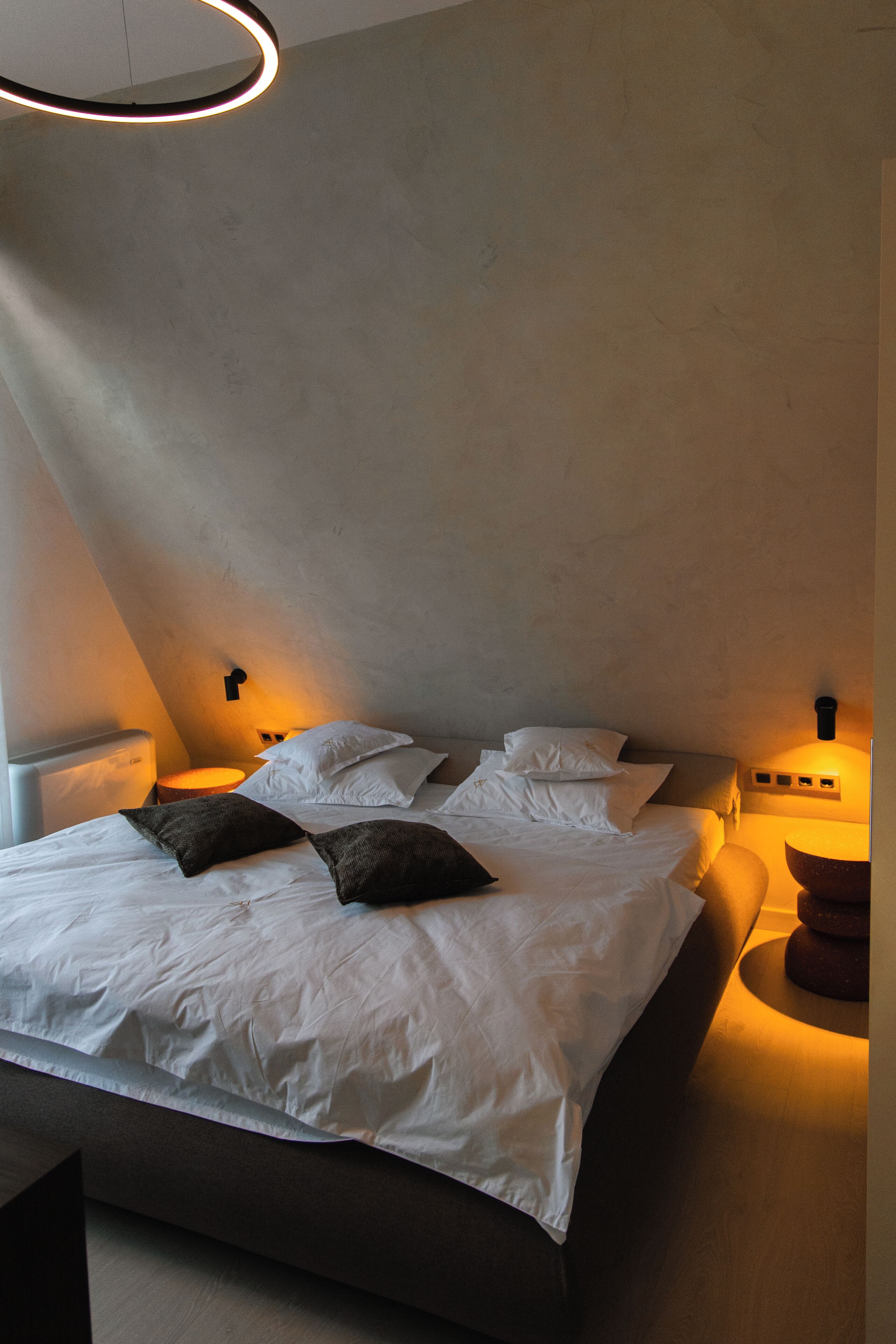 Un dormitorio moderno con cama, almohadas, lámparas de noche y una lámpara circular en el techo.