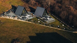 An aerial view of a modern building with a unique triangular roof design, surrounded by a landscaped area with pathways and spherical lights. - Twin Vista A-Frame Cabins (Sovata)