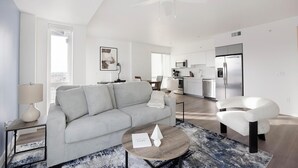 A modern living room with a sofa, coffee table, and a chair. There is a kitchen area with a refrigerator and microwave. - Landing | Stylish 2BD, Yoga Studio, Clubhouse (Tempe)