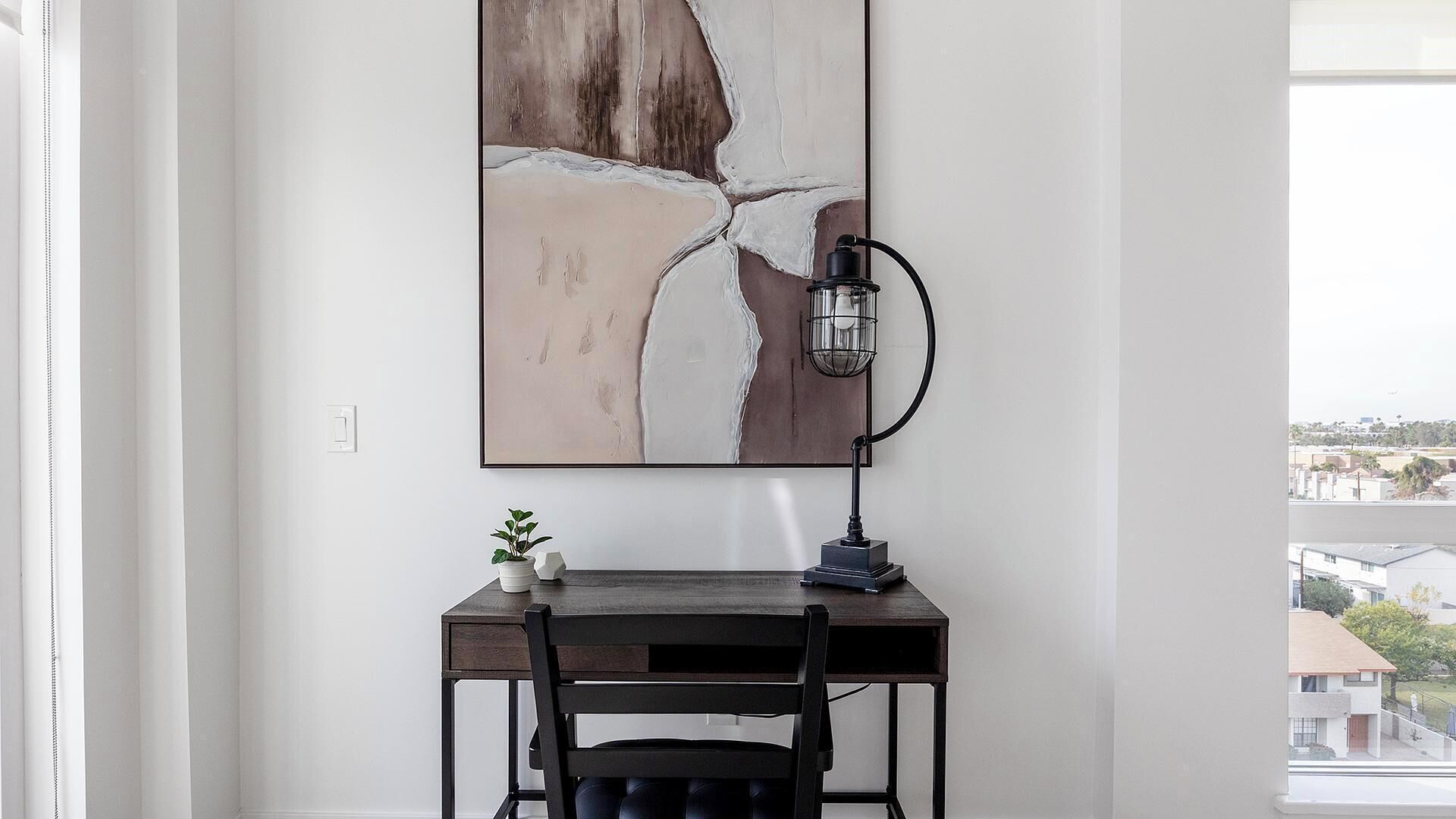 Una habitación moderna con escritorio, silla y un cuadro abstracto grande en la pared.