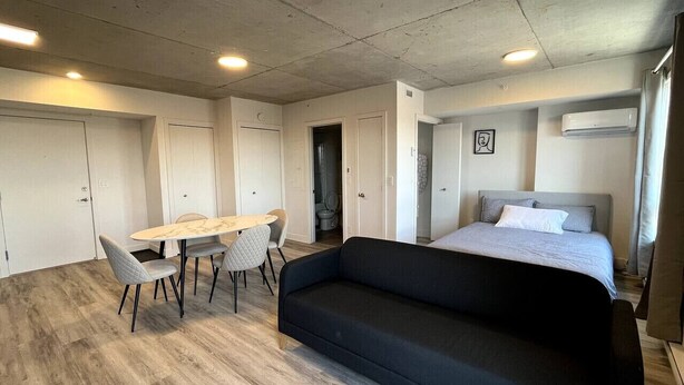 Una habitación moderna con cama, sofá, una mesa de comedor con sillas y una zona de kitchenette.