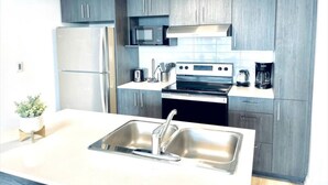A modern kitchen with grey cabinets, stainless steel appliances, and a central island with a sink. - Romema *201* - Condo Luxe 1 bdr (Montreal)