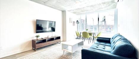 Uma sala de estar moderna com televisão de tela plana, um sofá, uma mesa de centro e uma área de jantar com cadeiras.