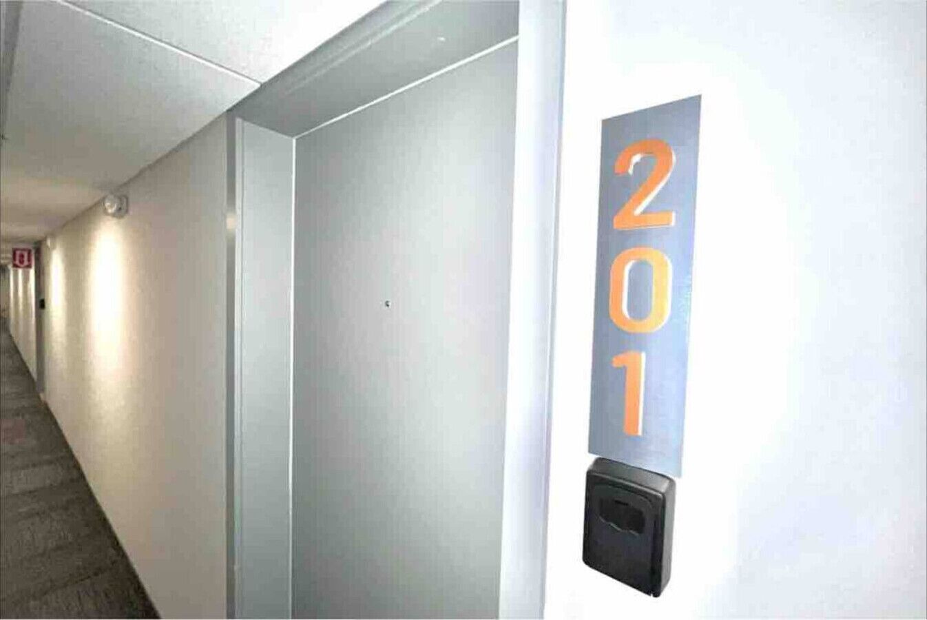 Un couloir avec une porte portant le numéro « 201 » et un détecteur d’incendie fixé au mur.