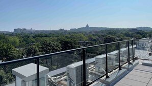 Una terrazza sul tetto con ringhiera in vetro che si affaccia su una vista panoramica della città, con una cupola imponente in evidenza.