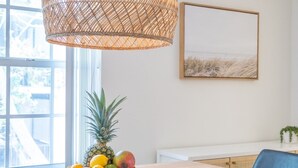 A dining area with a large woven pendant light, a bowl of fruit on the table, and a view through the window. - Beechwood  Suites  D (Sarasota)