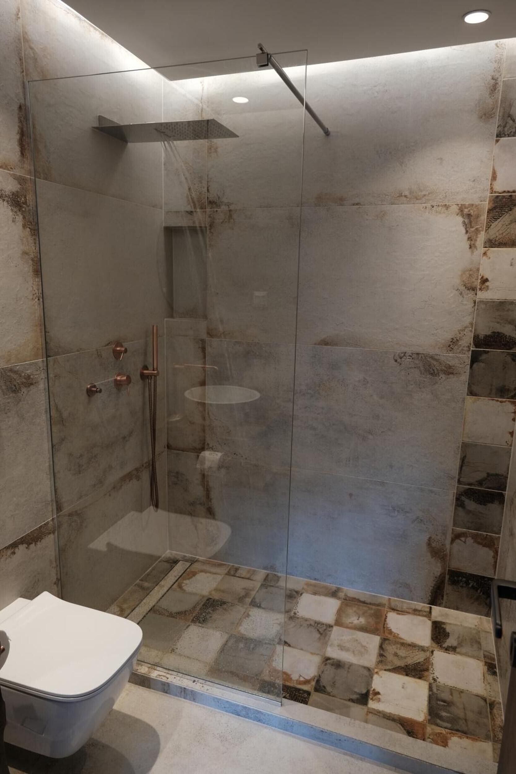 Eine begehbare Dusche mit Glaswänden, ein freistehendes WC und ein gefliester Boden.