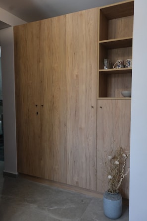 Une armoire en bois avec une étagère au-dessus, un vase contenant des fleurs séchées et un sol carrelé.