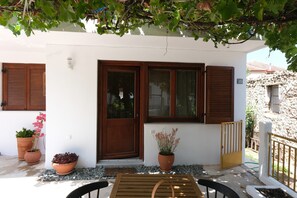 A white building with wooden shutters, potted plants, and a small outdoor seating area. - Apartment 'Villa Philia with Patio' with Mountain View, Wi-Fi and Air Conditioning (Litochoro)