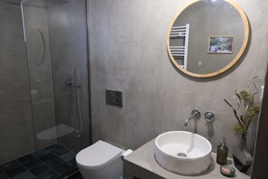 Ein modernes Badezimmer mit Duschkabine aus Glas, Toilette in Weiß, rundem Spiegel und Waschbecken mit einem Wasserhahn.