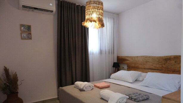 Habitación de hotel con una cama, cabecera de madera, mesita de noche, lámpara y planta en maceta.