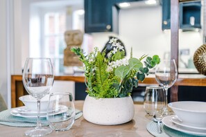 A dining table set with clear glassware, a white speckled bowl, and a potted plant with green foliage and white flowers. - Stunning Central York Apartments Sleep 18 (York)