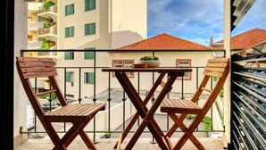 A balcony with wooden chairs and a table, overlooking a street and buildings with balconies. - Elvira's Corner, a Home in Madeira (Funchal)